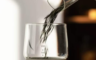 Pouring loose leaf tea into a measuring glass, demonstrating precision in tea preparation.