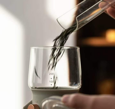 Pouring loose leaf tea into a measuring glass, demonstrating precision in tea preparation.