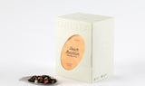 White Peach Oolong Tea box next to a display of its dried black tea leaves and peach pieces on a pristine white surface.