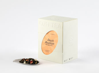 White Peach Oolong Tea box next to a display of its dried black tea leaves and peach pieces on a pristine white surface.