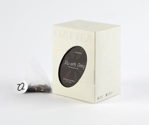 Packaging of Pu-erh Grey Tea with a peek of the tea bag, showcasing blended rose petals and dark tea leaves.