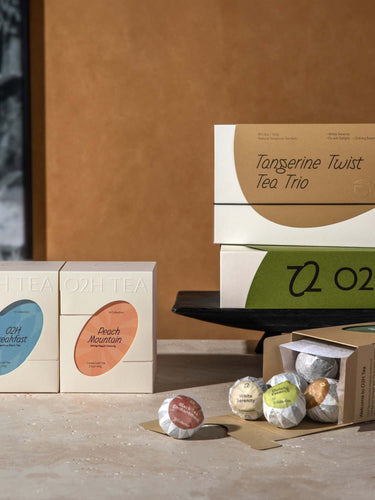 O2H Tea's gift sets, including Tangerine Twist Tea Trio, artistically presented on a modern table against an abstract art backdrop, embodying sophisticated gifting for tea enthusiasts.