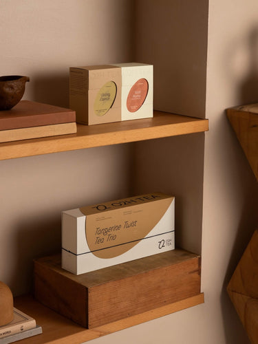O2H Tangerine Tea set elegantly displayed on a wooden shelf alongside artful pottery, enhancing the modern interior with a touch of sophistication.