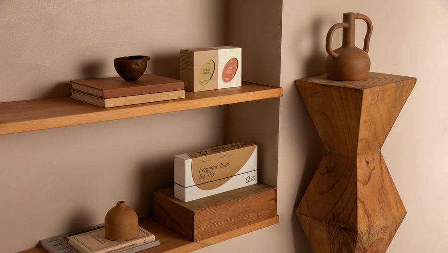 O2H Tangerine Tea set elegantly displayed on a wooden shelf alongside artful pottery, enhancing the modern interior with a touch of sophistication.