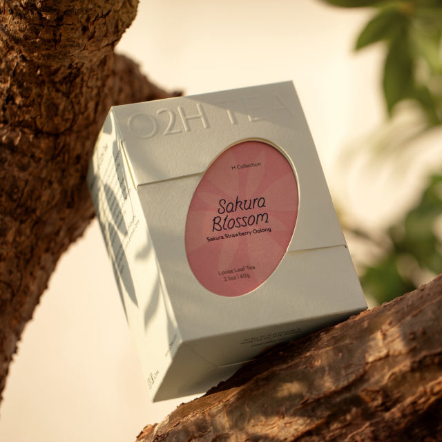 O2H Sakura Strawberry Oolong Tea elegantly packaged, perched on a tree branch, capturing the essence of its floral and fruity blend.